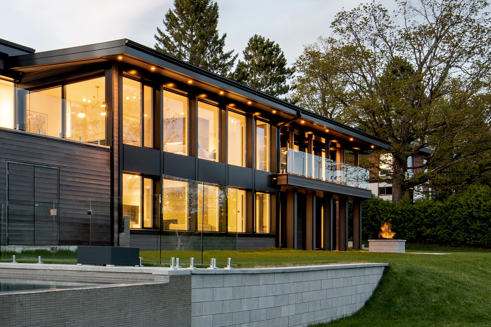 Maison contemporaine au crépuscule avec deux étages de grandes fenêtres en aluminium noir éclairées