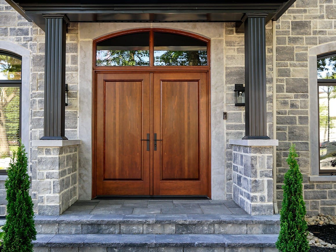 Double porte d’entrée en bois Lepage Millwork avec imposte cintrée, sous un portique de maison en pierre