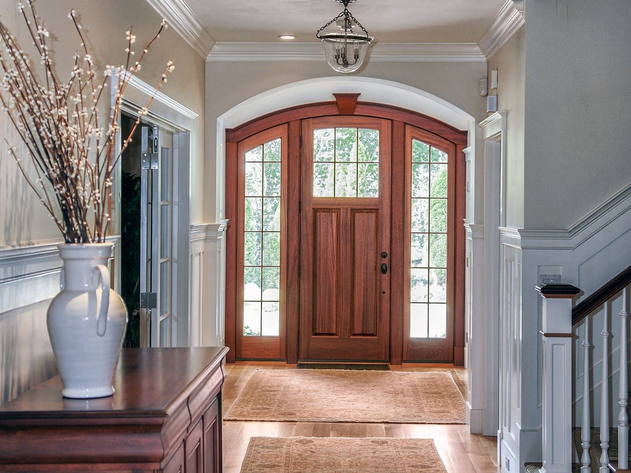 Porte d’entrée en bois cintrée avec latéraux vitrés, au bout d’un hall d’entrée classique