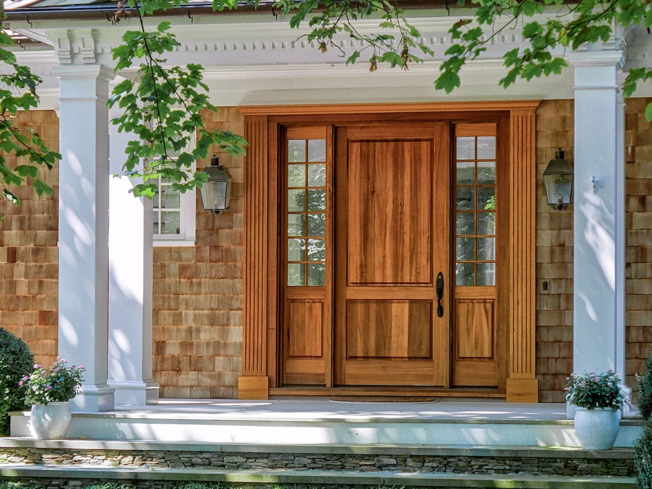 Porte d’entrée en bois naturel Lepage Millwork avec deux latéraux vitrés, sous un portique à colonnes blanches