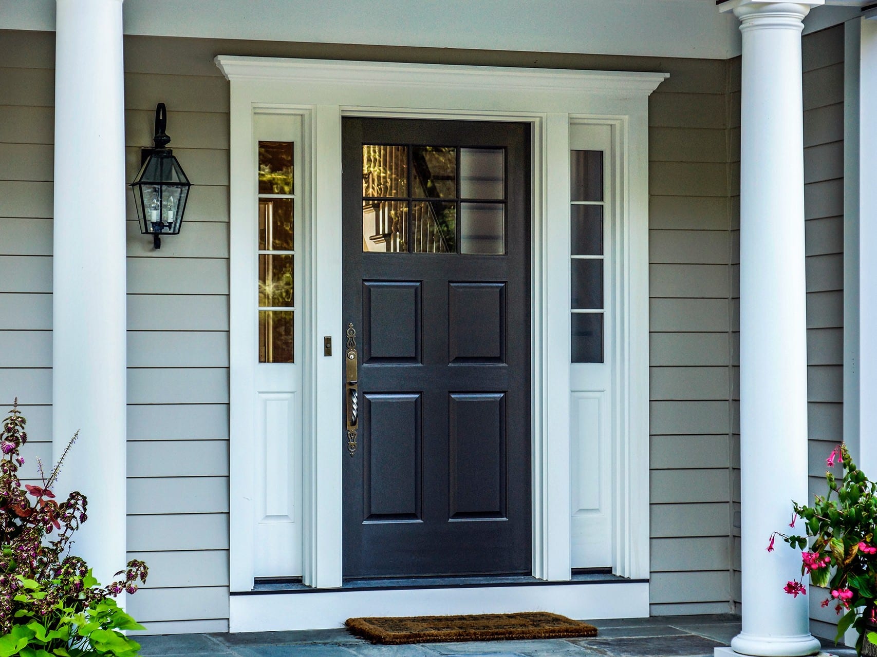 Black Lepage Millwork entry door with a divided upper glass lite, two white sidelites and a brass-toned handle, under a columned porch