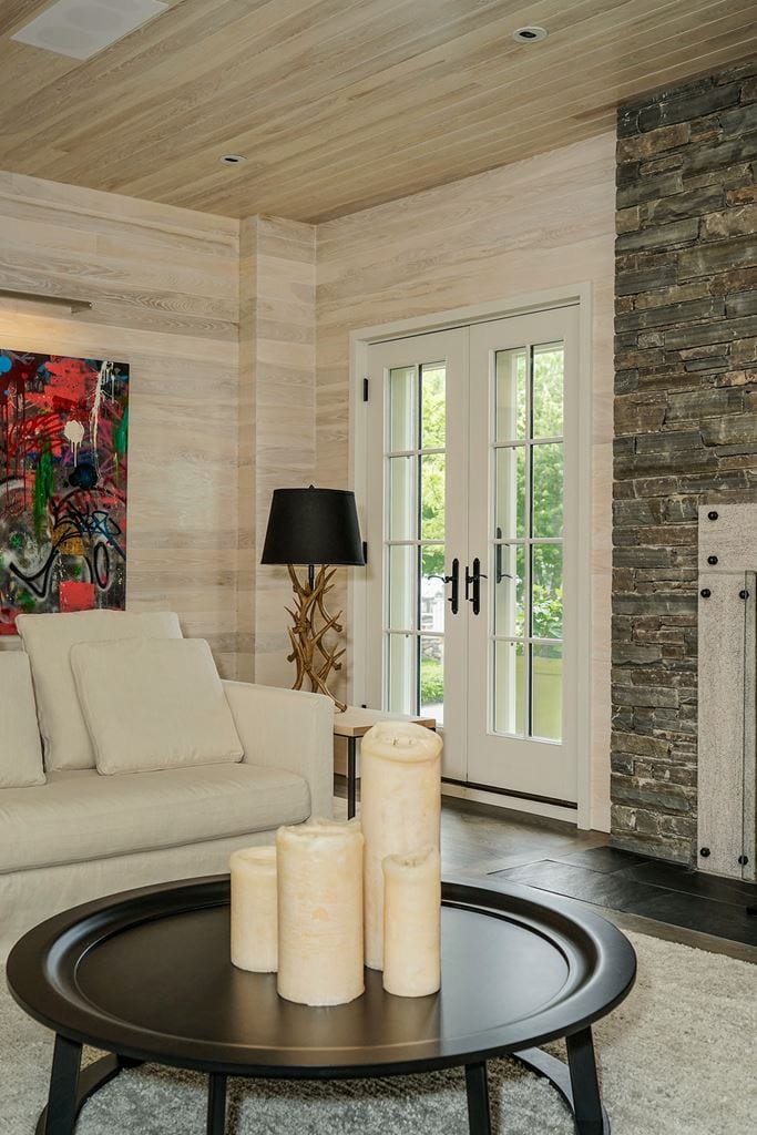 White French door in a living room panelled in whitewashed wood, with a stone fireplace